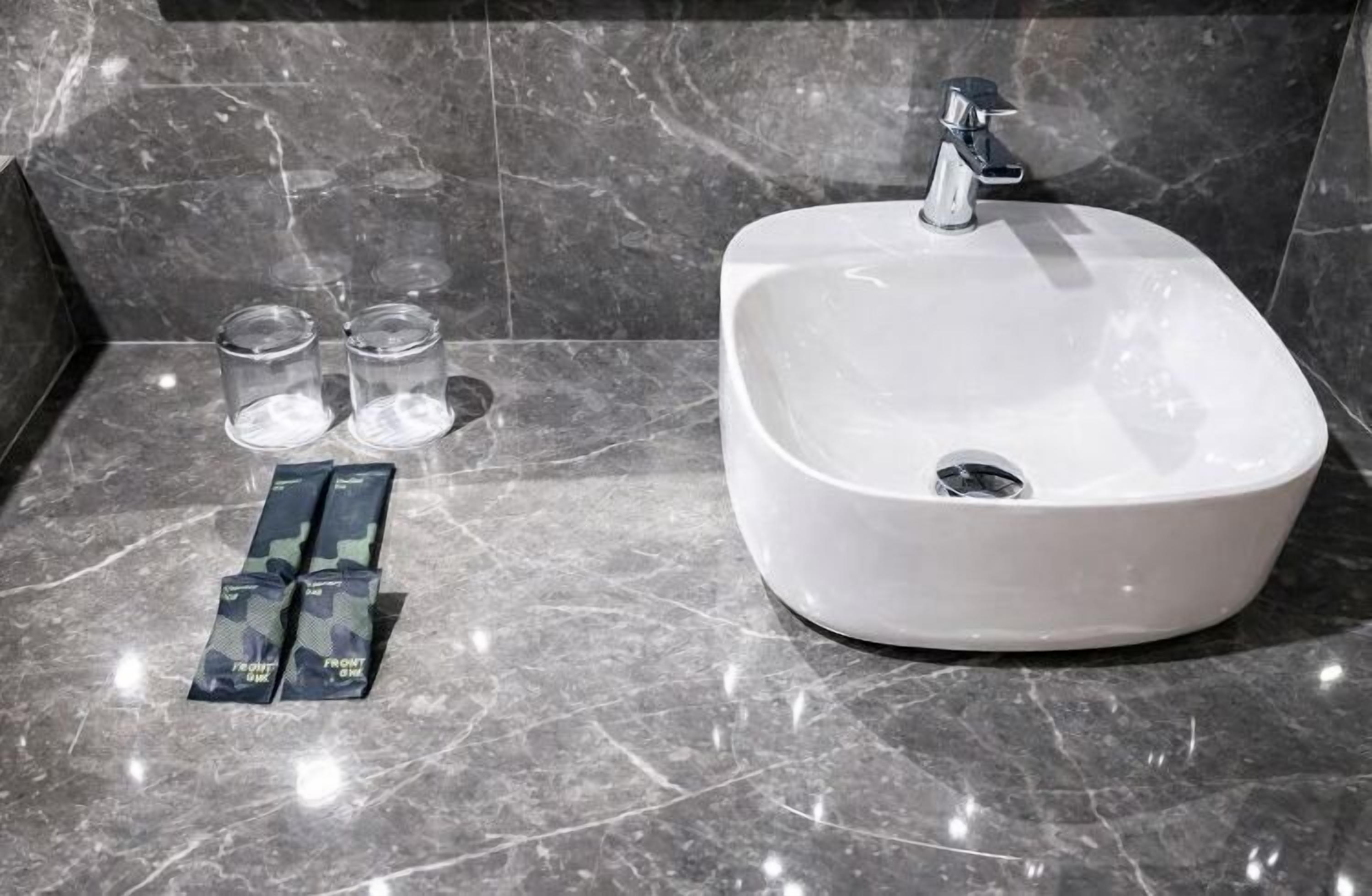 A bathroom with a white sink, a modern faucet, and three small glasses on the counter.
