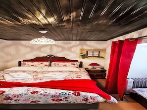 Ein Schlafzimmer mit Holzboden, einem Bett mit floralem Bettbezug, einem Nachttisch mit Lampe und einem Heizkörper.