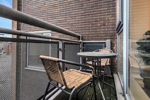 A balcony with a metal railing, a small round table, two wicker chairs, and a mesh screen.