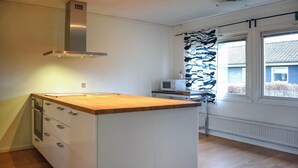 Et køkken med træbordplade, hvide skabe, stinkende emfang i rustfrit stål, en mikrobølgeovn og et vindue med udsigt til et hus.