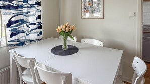 Et spisebord med en vase blomster, hvide stole og en stribet gardin.