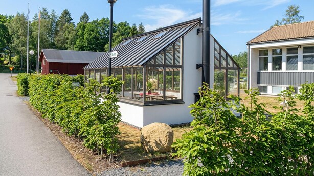En moderne drivhuskonstruktion i glas med ståltag, en skorsten og en lille tilbygning med tagsten.