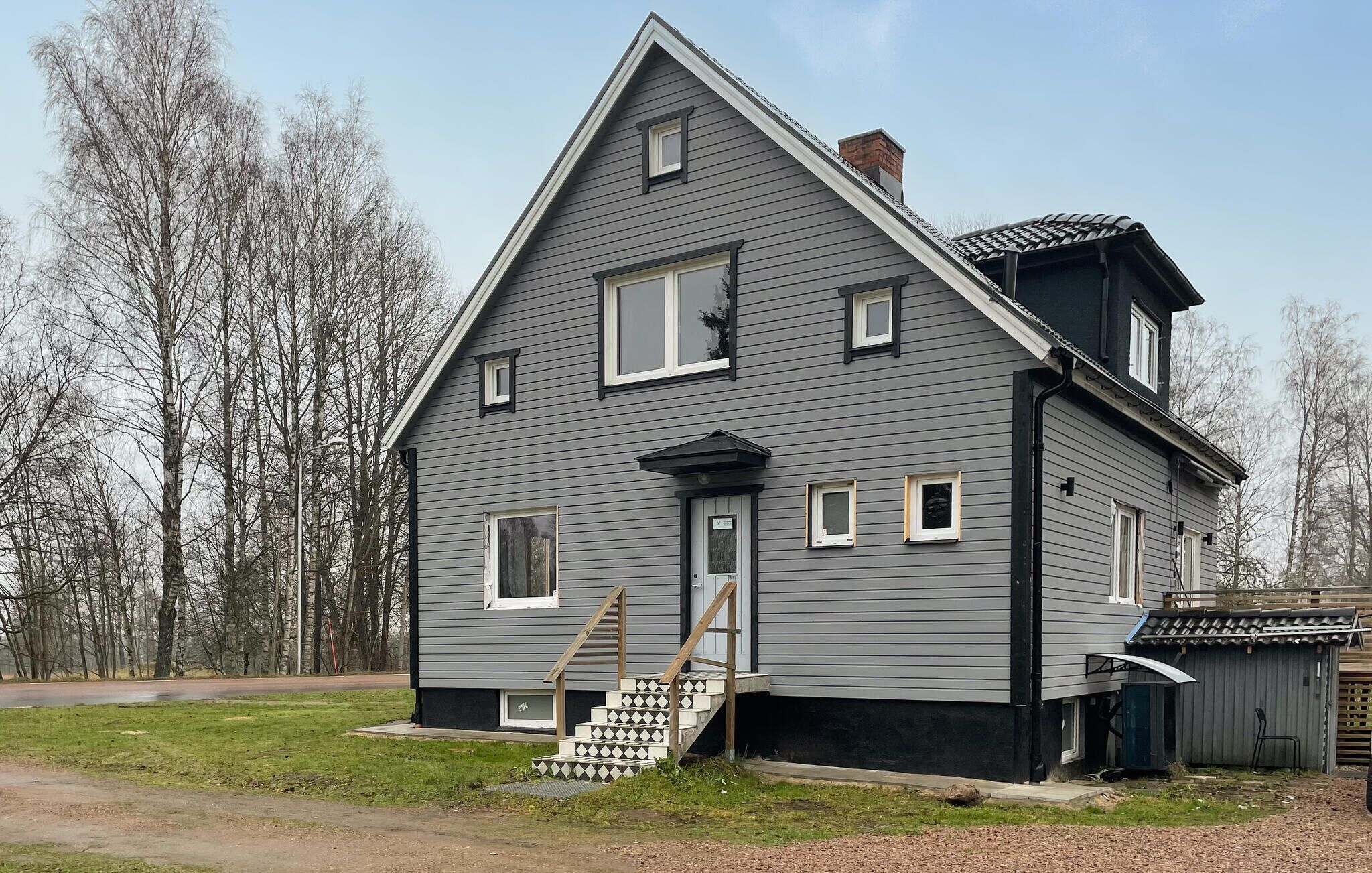 A two-story house with a steep gable roof, a front porch with a staircase, and a garage attached to the right side.