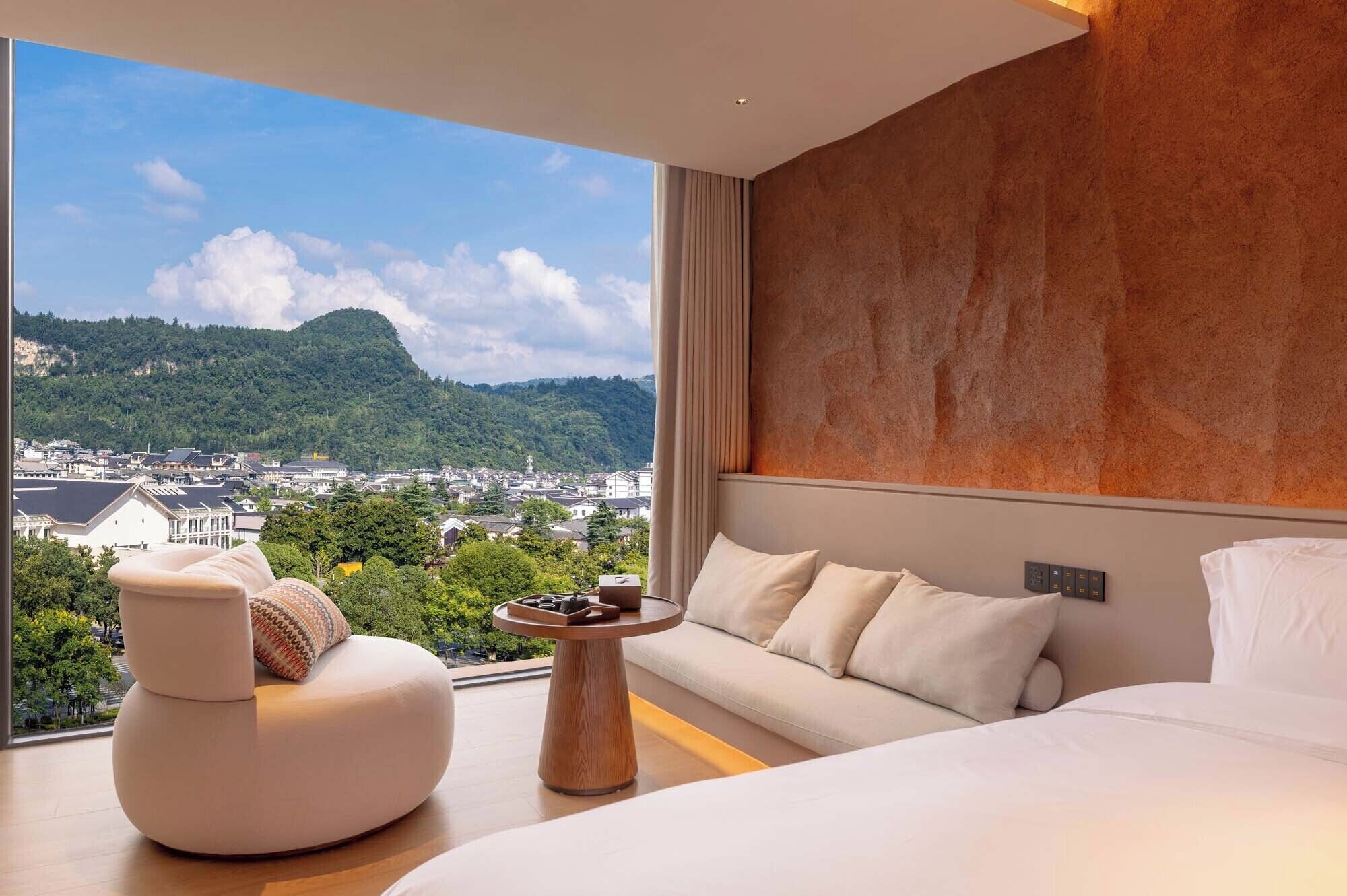 Ett modernt hotellrum med ett stort fönster som erbjuder en vacker utsikt över en stad och berg.