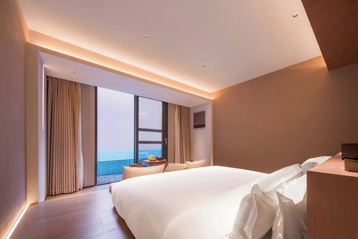 Ett modernt hotellrum med en stor säng, en liten sittgrupp och utsikt över havet genom stora fönster.