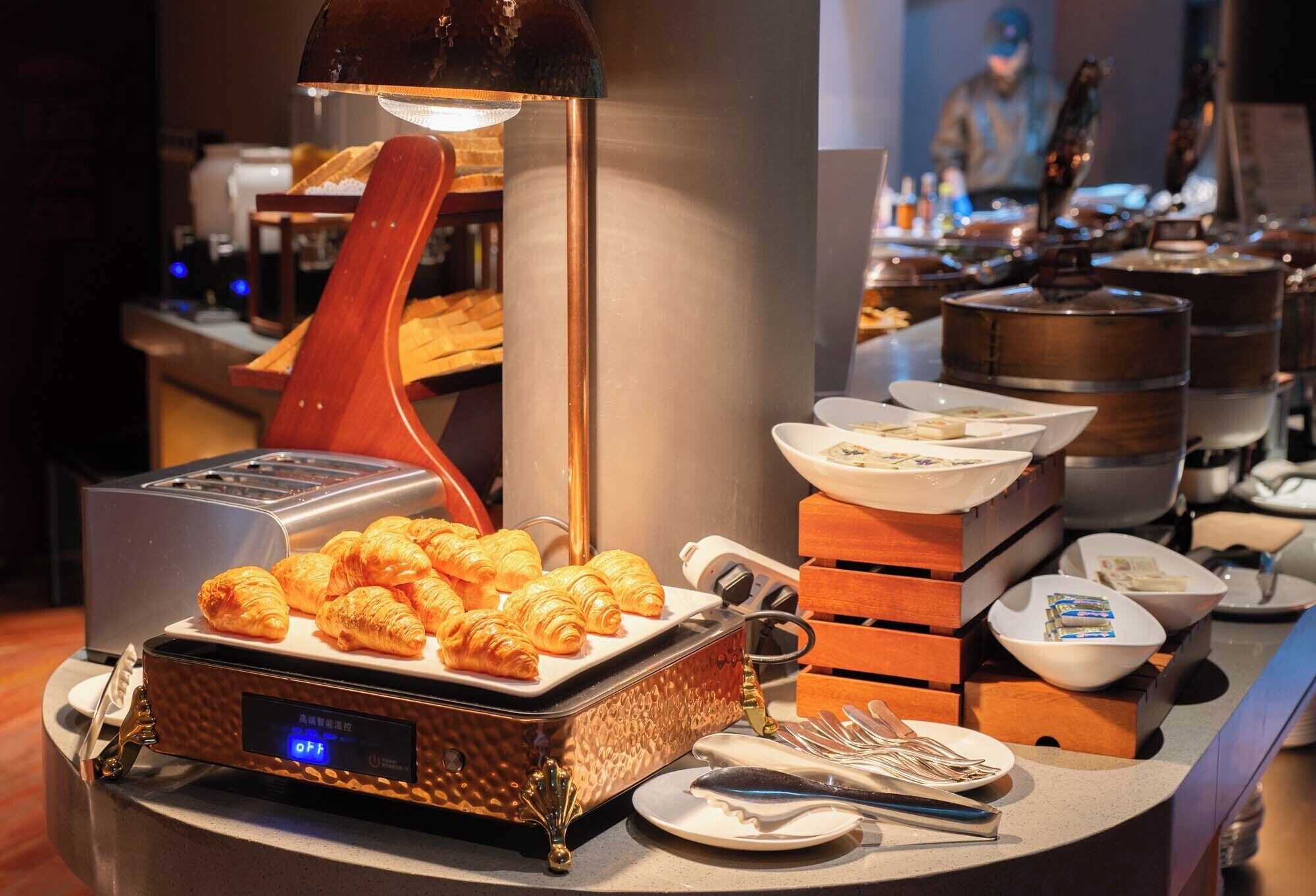 Een ontbijtbuffet met croissants, schalen vol eten en bestek.