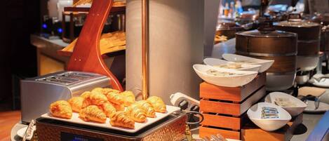 Een ontbijtbuffet met croissants, schalen vol eten en bestek.