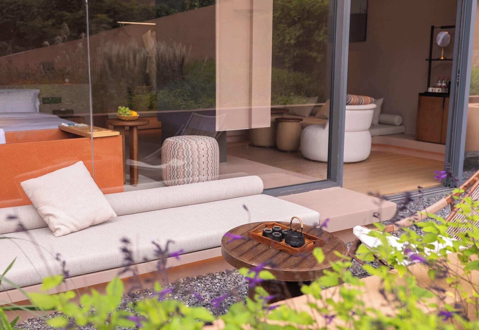 A modern living room with a sofa, a round wooden coffee table, and a glass wall offering a view of the outdoors.