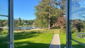 A view through glass doors of a grassy area with a path leading to a body of water, surrounded by trees and houses.