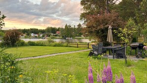 A grassy outdoor area with a table and chairs, a barbecue grill, and a path leading to a body of water.