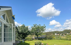 Uma casa com uma janela grande e uma bandeira, cercada por um jardim exuberante e um lago.