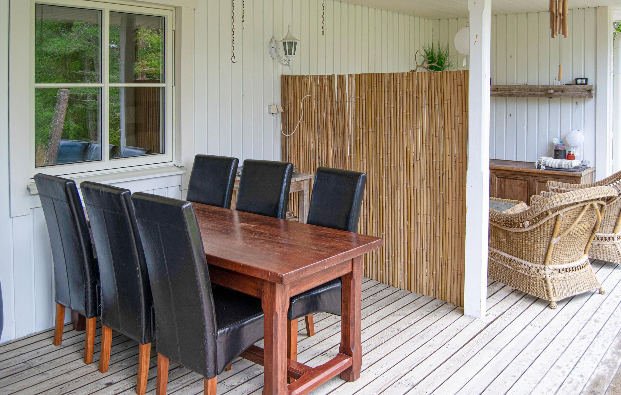 Eine Holzterrasse mit Esstisch und Stühlen, ein Bambus Sichtschutz, Korbmöbel und eine weiße Außenwand.
