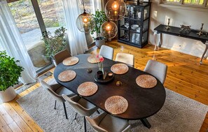 Un coin repas avec une table en bois foncé, des sets de table en fibres tressées et un éclairage moderne suspendu au plafond.