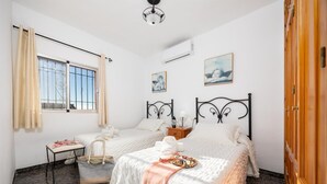 Un dormitorio con dos camas, una ventana con cortinas, una mesa con silla y una obra de arte en la pared.