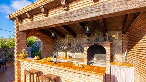 Un área de bar al aire libre con chimenea de piedra, taburetes de madera y piso de baldosas.