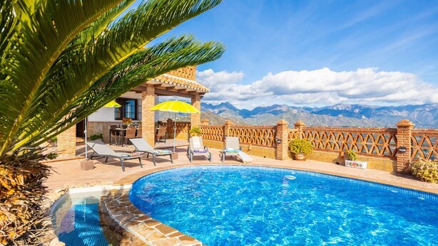 A pool area with lounge chairs and umbrellas, a brick wall, and a view of mountains. - Villa Baena in Macaca (Torrox)