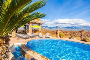 A pool area with lounge chairs and umbrellas, a brick wall, and a view of mountains. - Villa Baena in Macaca (Torrox)
