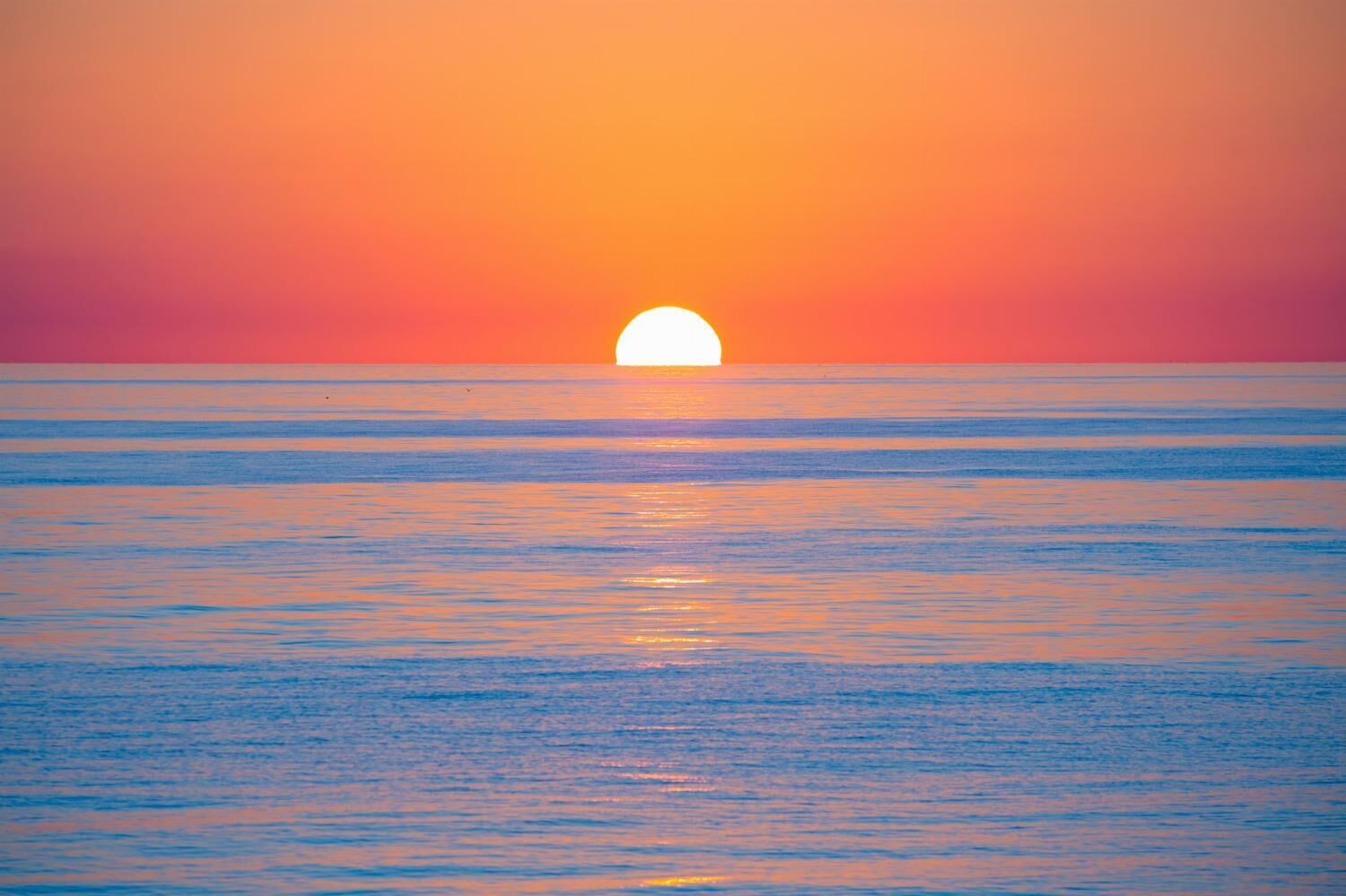 A sunset over a calm sea with a clear horizon.