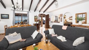 A spacious living room with dark grey sofas, a wooden coffee table, and a dining area in the background. - Villa Baena in Macaca (Torrox)