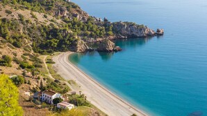 A coastal landscape with a beach, a path leading to a building, and a rocky outcrop with a tower. - Villa Baena in Macaca (Torrox)