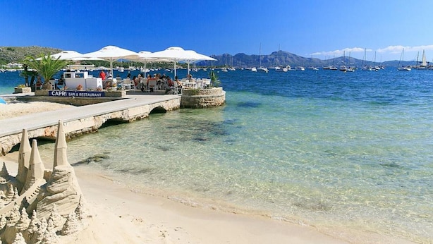 A coastal scene with a bar and restaurant named 'CAPRI' on a pier, clear blue water, and boats in the distance. - Villa Gosp Torres in Mallorca (Alcúdia)