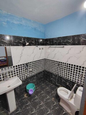 A bathroom with a sink, toilet, and shower. The walls are tiled with black and white marble patterns. - Brother's In Mountains (Kasol)