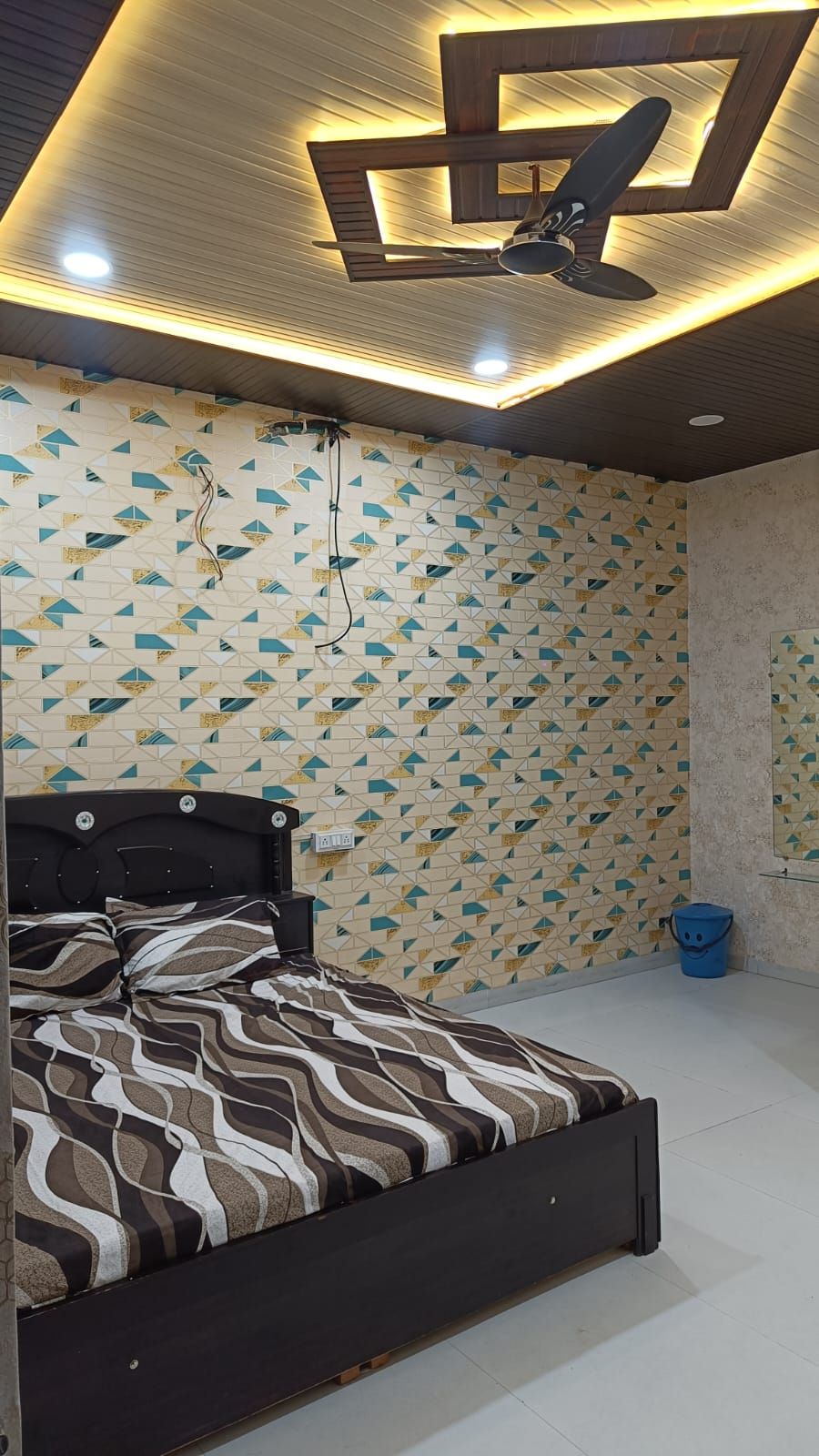 A bedroom with a bed, patterned wallpaper, a ceiling light fixture, and a blue bucket.