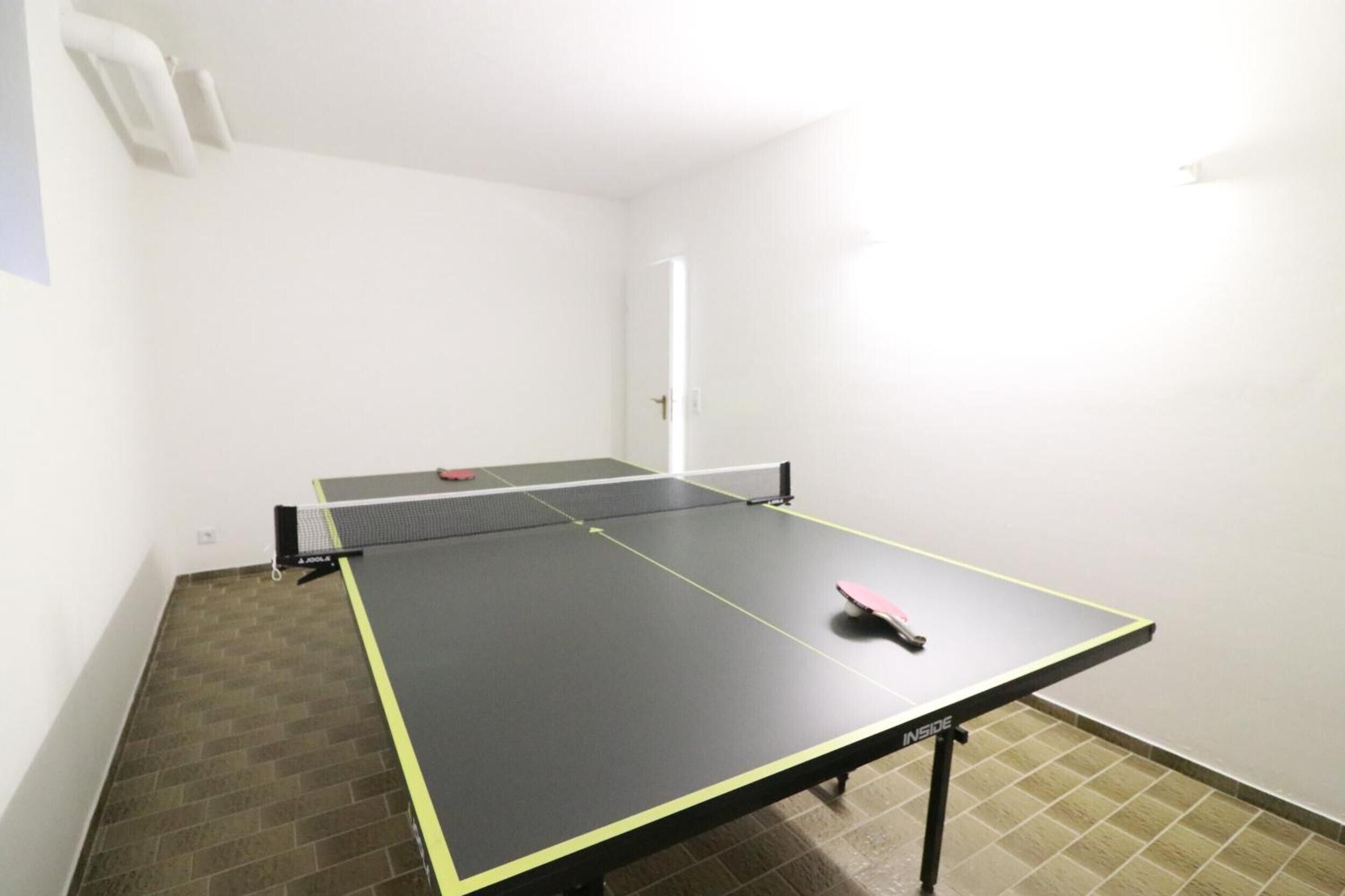 Et ping pong-bord i et rum med en dør og et flisebelagt gulv.