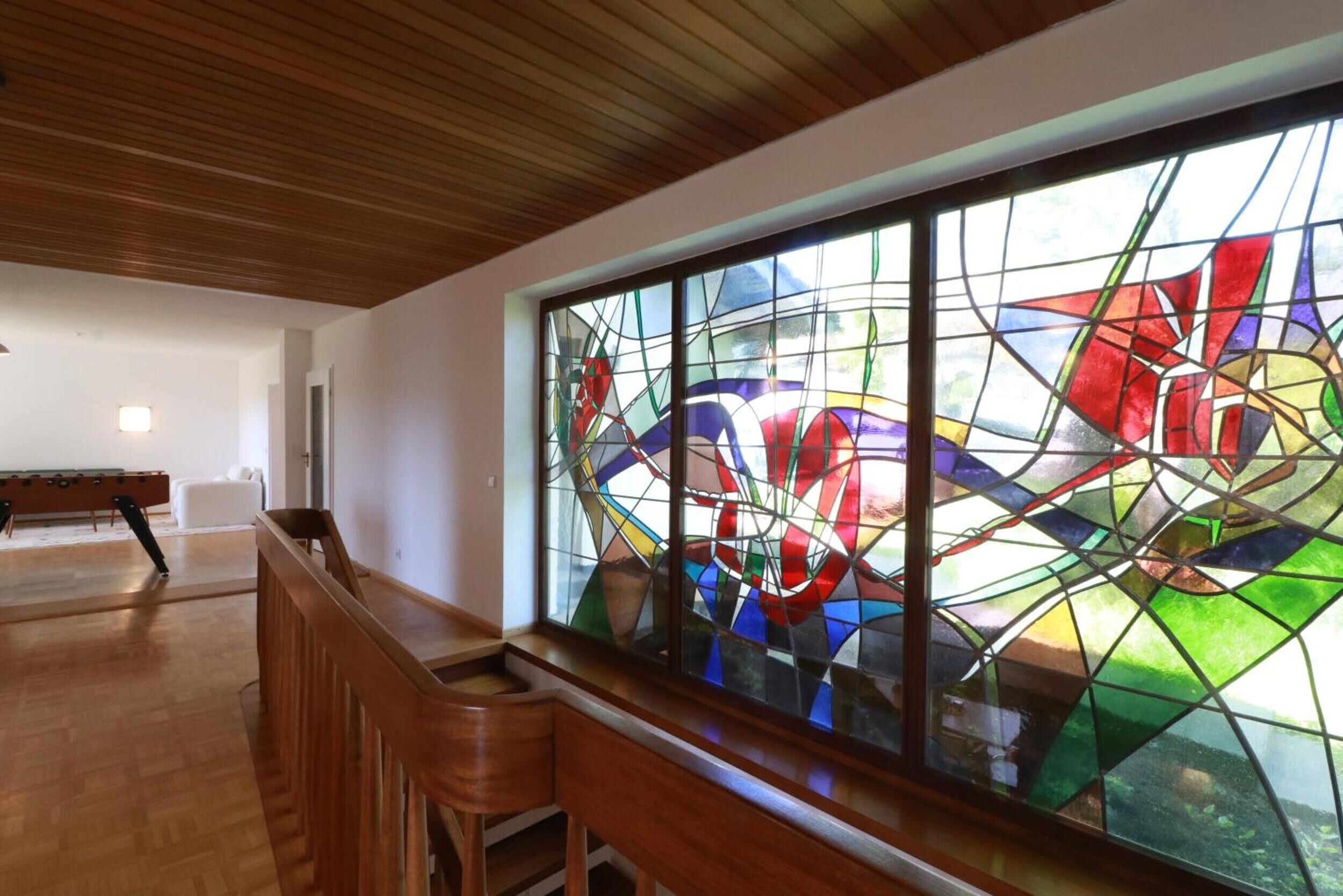 A room with a wooden bench, a large stained glass window, and a wooden ceiling.