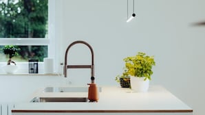 Une cuisine moderne dotée d’un îlot central, d’un robinet en cuivre et d’un luminaire suspendu.