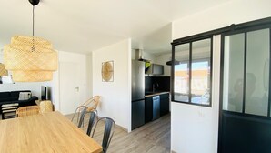 Eine moderne Küche mit schwarzen Schränken, einem eingebauten Backofen und einem Geschirrspüler. Es gibt einen Essbereich mit einem Holztisch und Stühlen sowie ein großes Fenster mit Blick nach draußen.