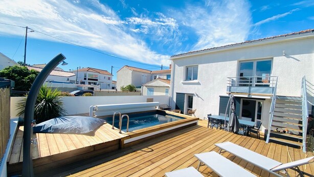 Eine Holzterrasse mit Pool, Liegestühlen und einer Treppe zu einem Balkon.