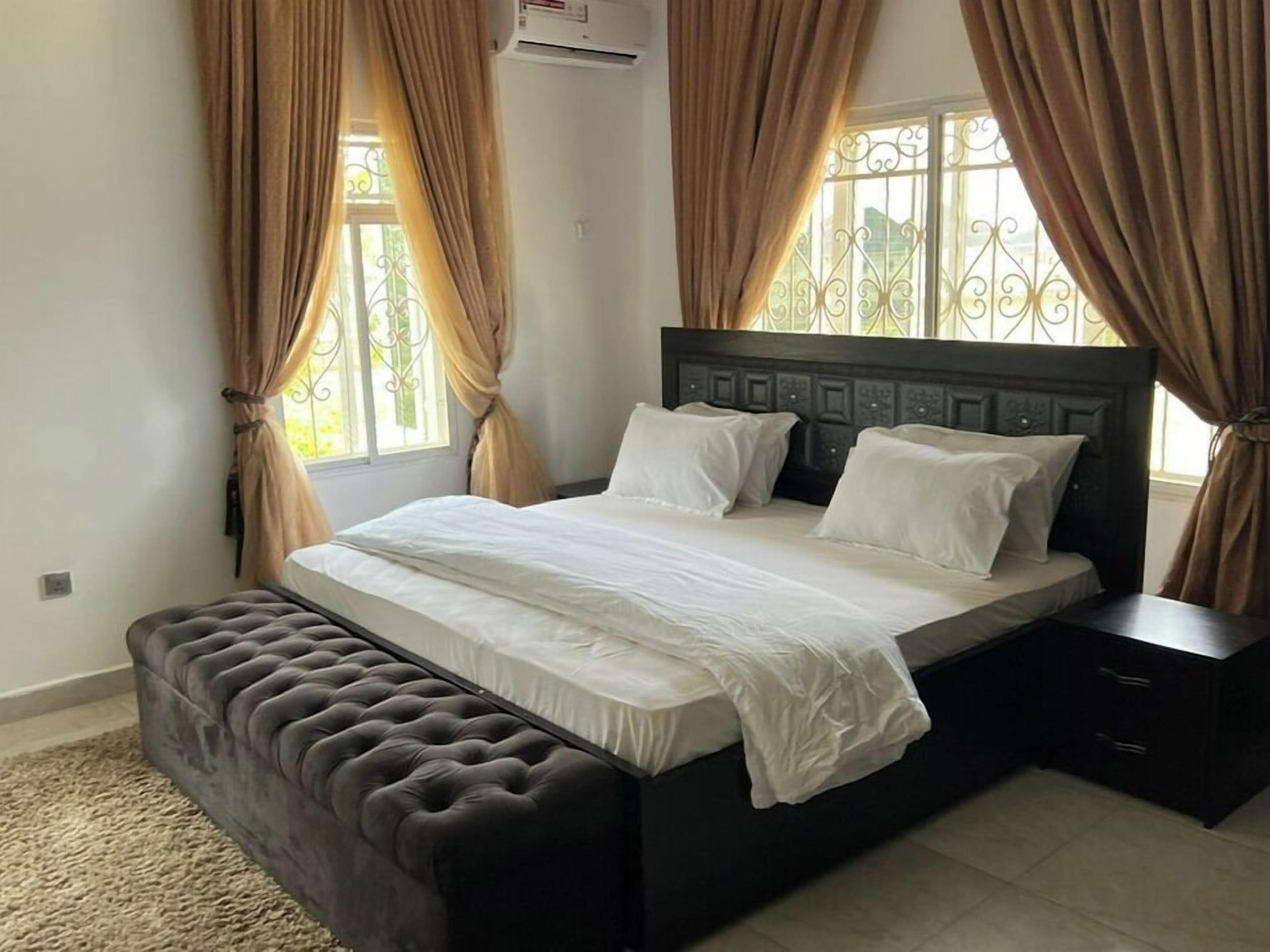 Une chambre à coucher avec un grand lit, une tête de lit sombre et un banc au pied du lit.