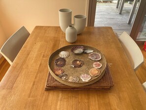A wooden dining table with a woven placemat holding a decorative plate of seashells.