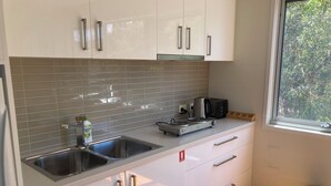 A modern kitchen with white cabinets, a stainless steel sink, a toaster, and a kettle. - 20 Bradley (Coles Bay)