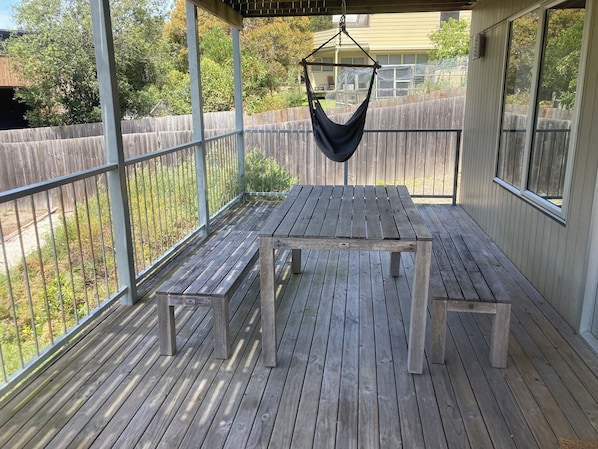 A covered wooden deck with a table and benches, surrounded by a metal railing and a wooden fence. - 20 Bradley (Coles Bay)