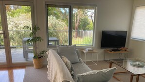 A living room with a sofa, a TV, a glass table, and a potted plant. - 20 Bradley (Coles Bay)