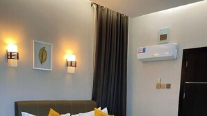 A hotel room with a large bed, two bedside lamps, a wall-mounted air conditioner, and a door. - Lavish Apartment (Abuja)