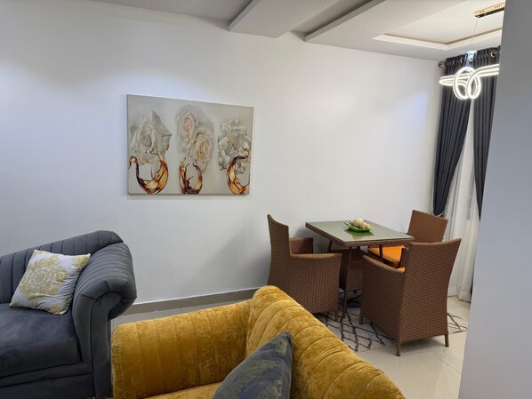 Un salon moderne avec un canapé gris, un canapé jaune et une table à manger entourée de chaises en osier.