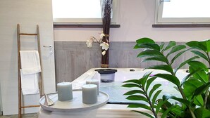 Ein Wellnessbereich mit Whirlpool, Kerzen, einem Handtuchhalter und einer Pflanze.
