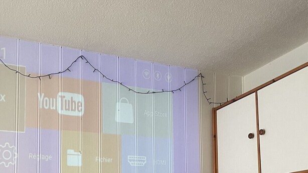 A bedroom with a bed, a grey sofa, a wooden headboard, and a projection screen displaying icons. - Nice Apt for 4 pers mountain view (Morillon)