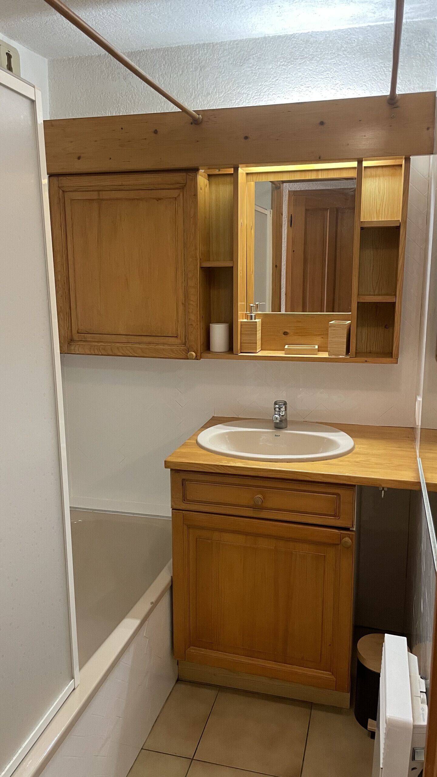 A compact bathroom with a wooden vanity, a sink, a mirror, and a toilet.