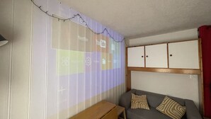 A room with a projection screen displaying various icons, a grey sofa with patterned cushions, and a wooden cabinet above the sofa. - Nice Apt for 4 pers mountain view (Morillon)