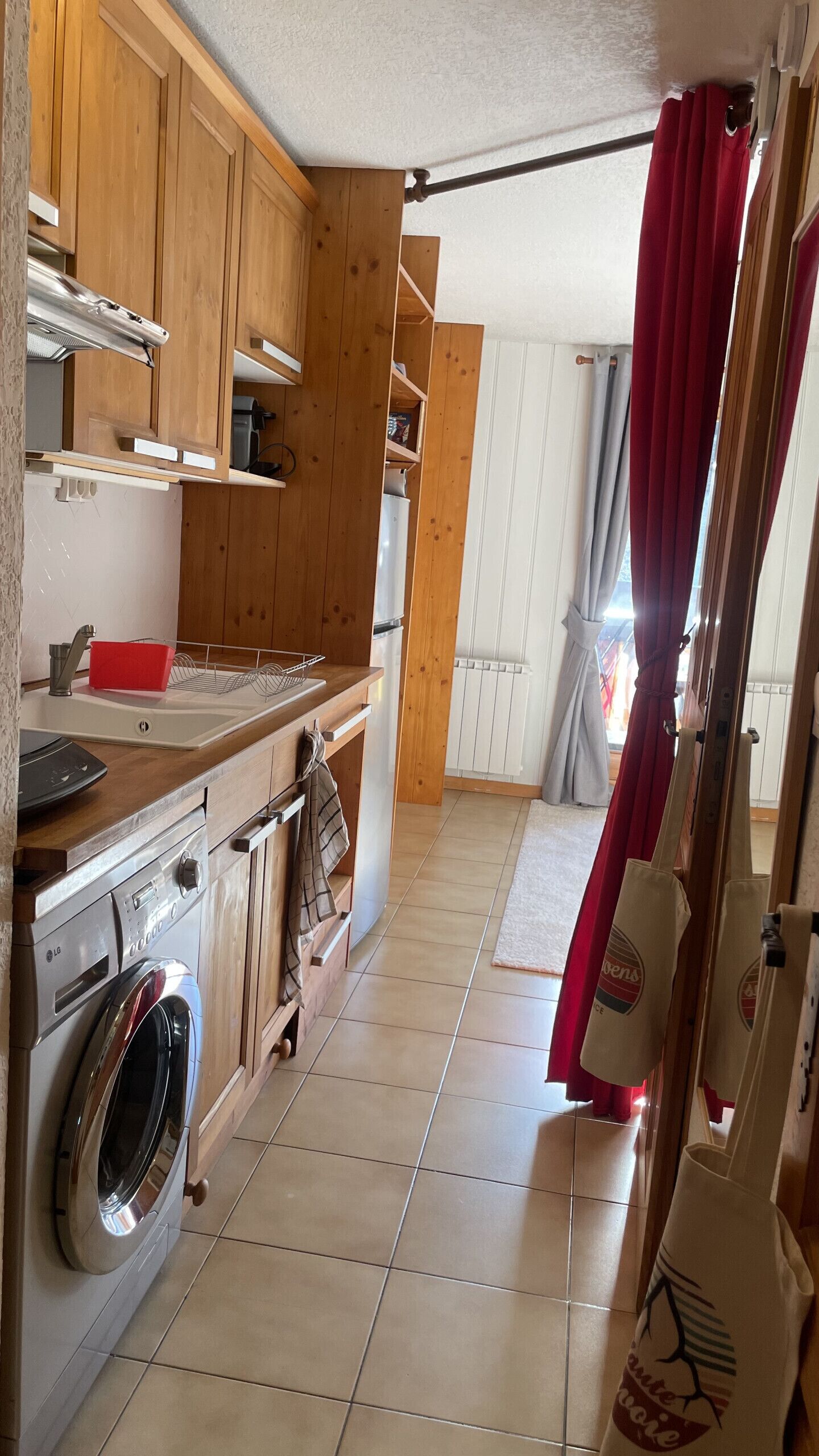 Une cuisine avec des meubles en bois, un lave-linge et un rideau rouge.
