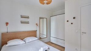 Una habitación de hotel moderna con cabecera de madera, cama grande con ropa blanca, mesita de noche con lámpara, armario y espejo.
