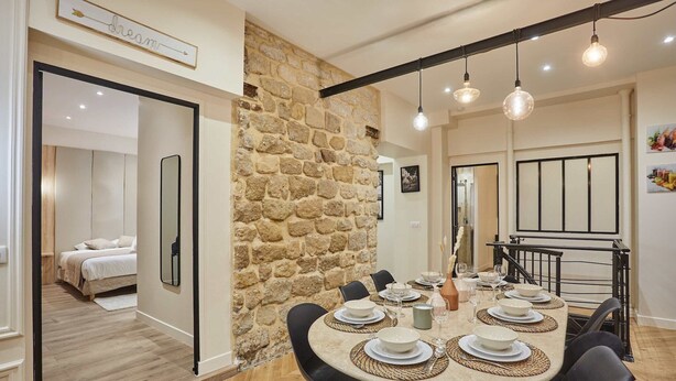 A dining area with a stone wall, a round table set for six, and a black metal railing. - Sublime apartment in the heart of Paris 10 people (Paris)
