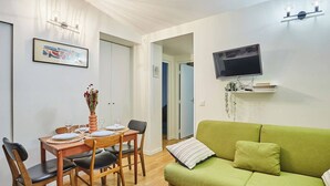 A dining area with a wooden table set for four, a green sofa, and a flat-screen TV mounted on the wall. - Charming  Duplex Le Marais/Beaubourg (Paris)