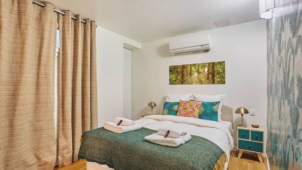 A neatly made bed with a green and white bedspread, two towels, and a painting of a forested bridge on the wall. - Charming  Duplex Le Marais/Beaubourg (Paris)