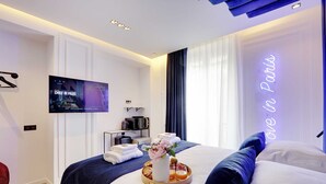 Een moderne hotelkamer met een bed, een televisie, een dienblad met ontbijt en een neonbord.