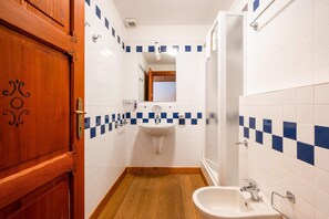 Un baño con puerta de madera, paredes con azulejos blancos, un lavamanos y un espejo.